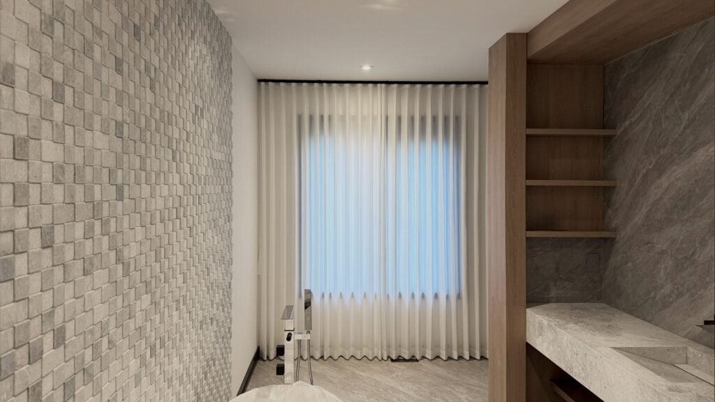 Moisture-resistant sheer curtains installed over a large window in a luxury marble bathroom.