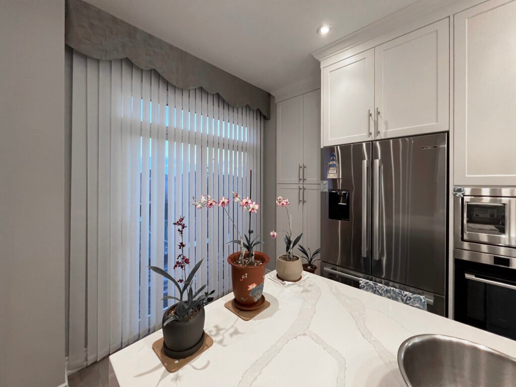 Sleek modern kitchen with white vertical blinds and a matching grey scalloped fabric valance on patio doors next to stainless steel appliances.