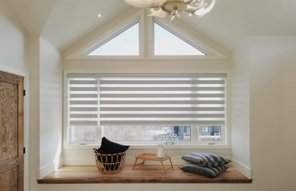 Modern white horizontal blinds installed on a wide window beneath a wooden window seat bench and architectural triangular transom windows.