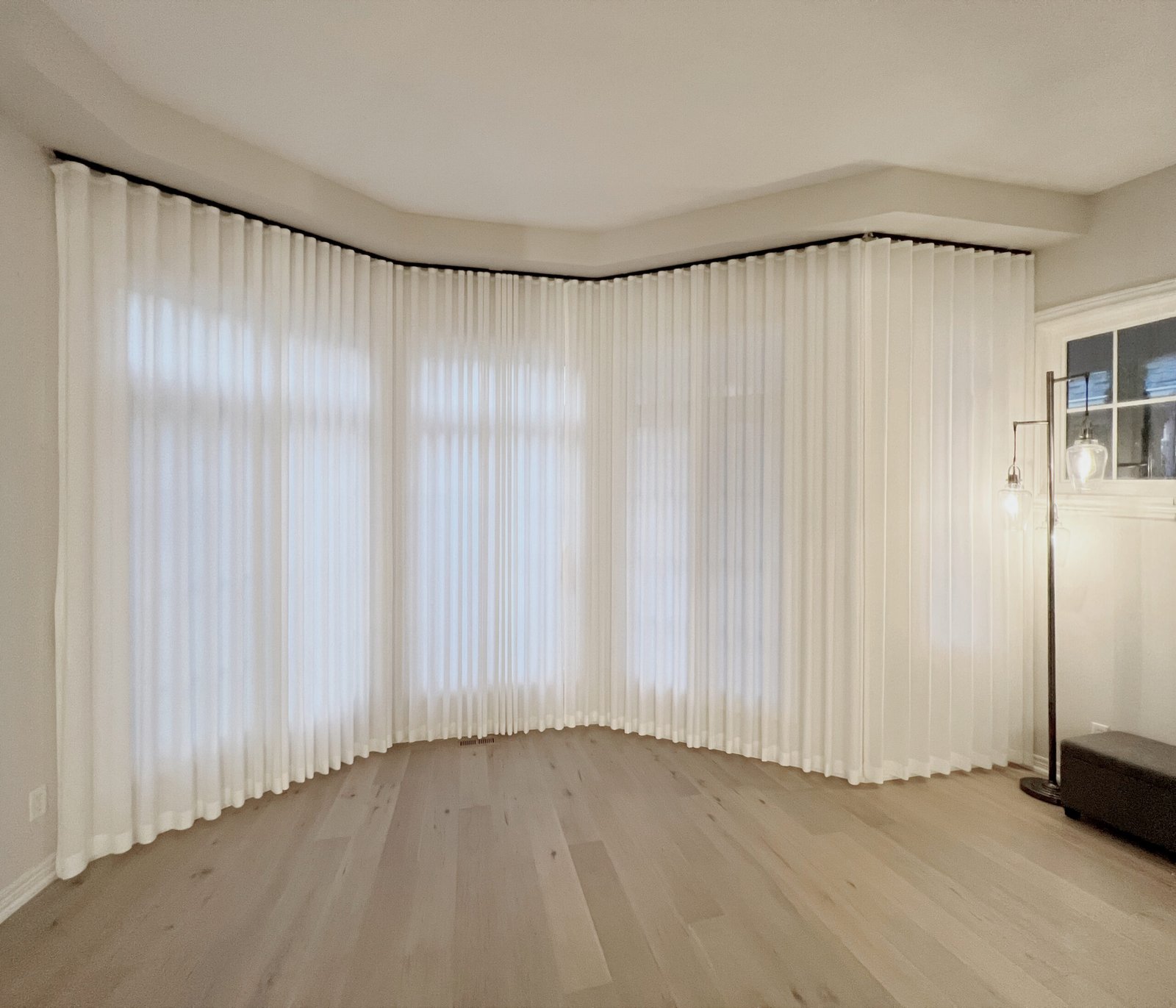 Curved bay window in a Toronto home dressed with floor-to-ceiling sheer curtains on a custom curved ceiling-mounted track — Starlight Shutter installation