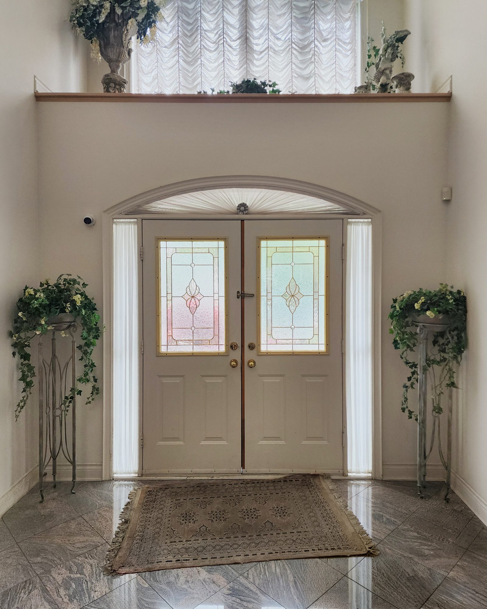 Grand Toronto entry foyer with fan-pleated arch shade above the front door, sidelite sheers, and transom treatment above — Starlight Shutter full door surround installation