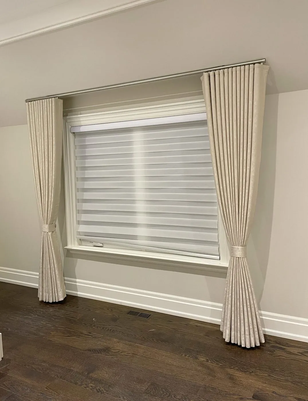 Zebra blind layered with blackout pinch-pleat drapes in a Toronto bedroom