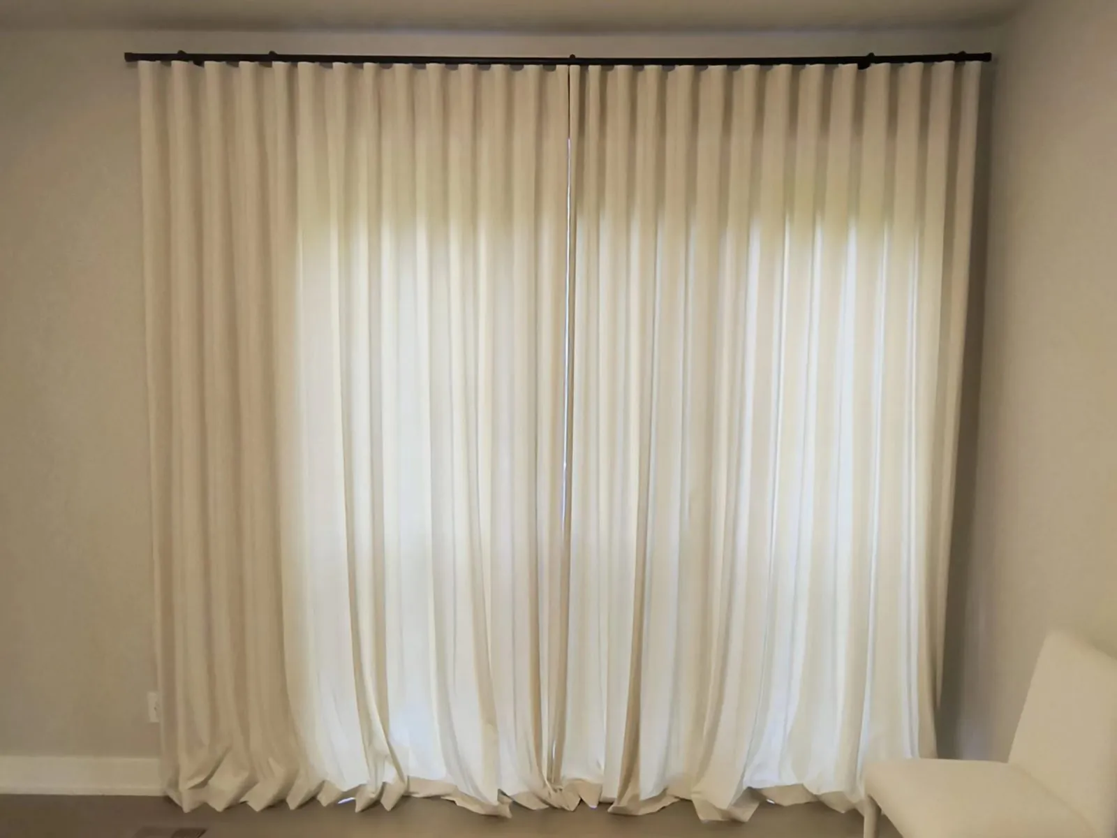 Cream linen curtains drawn across a window with warm light glowing through the weave
