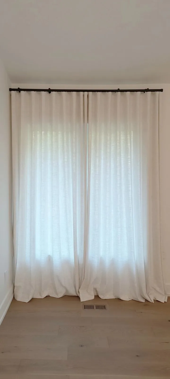 Natural linen drapery with a soft puddle hem pooling at a light wood floor