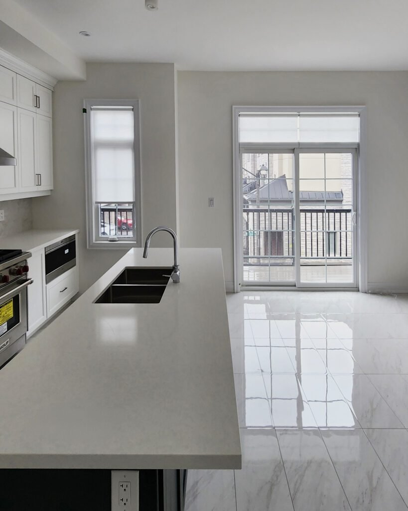 Minimalist white roller blinds installed on a kitchen window and matching sliding patio doors next to a marble island.