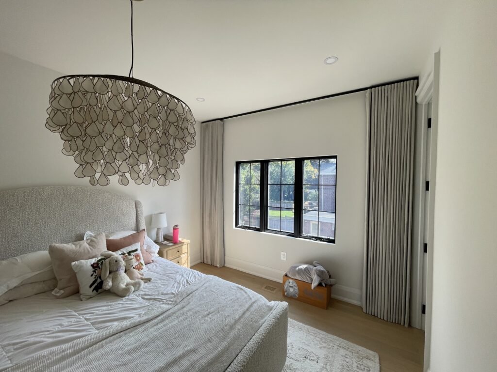 Elegant floor-to-ceiling custom ripple fold drapery in a modern cream bedroom, framing a black window frame.