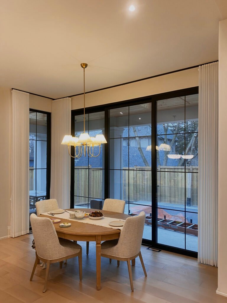 Tailored white ripple-fold drapery panels framing black-trimmed glass patio doors in a stylish dining room.