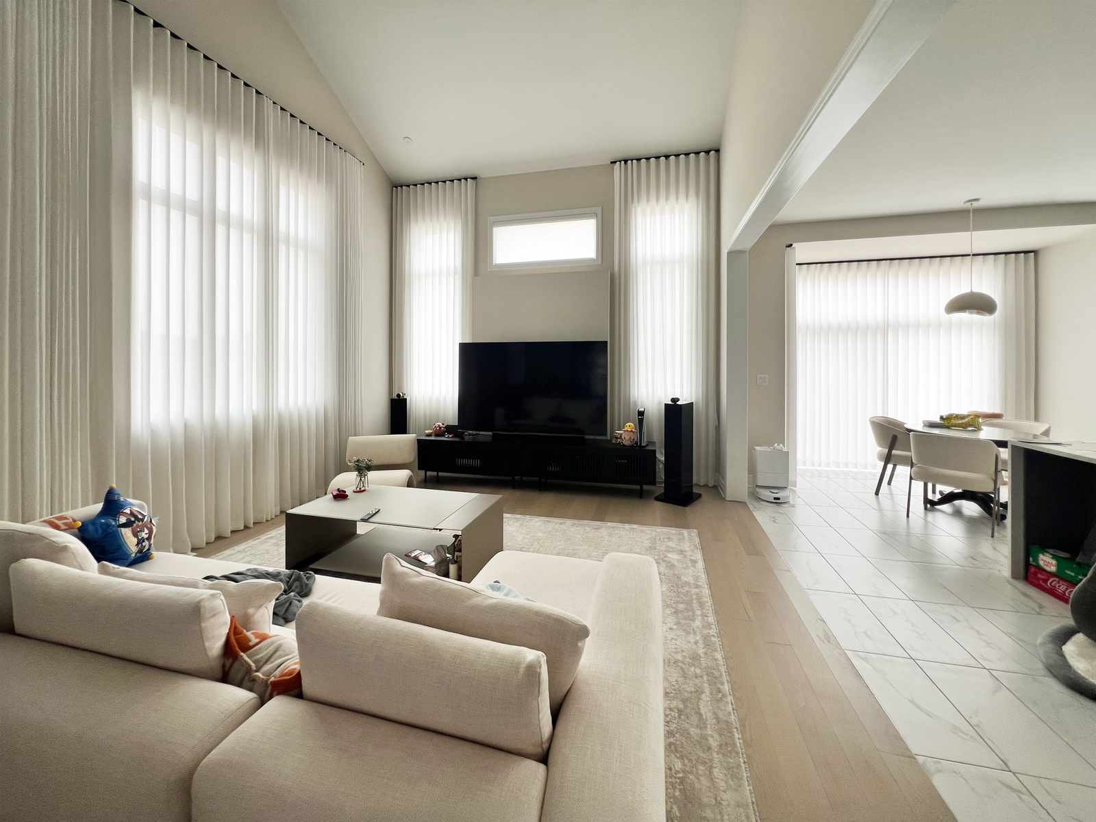 Floor-to-ceiling white ripple-fold curtains installed on high-ceiling windows in a modern living and dining area.