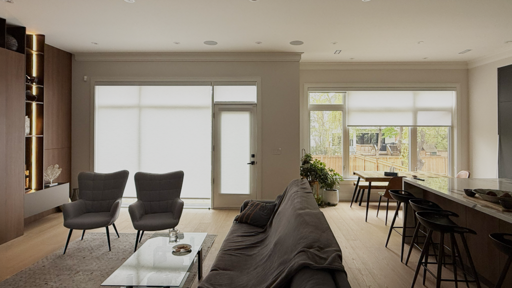 Custom light-filtering roller blinds covering large windows and a patio door in an open-concept living and dining space.