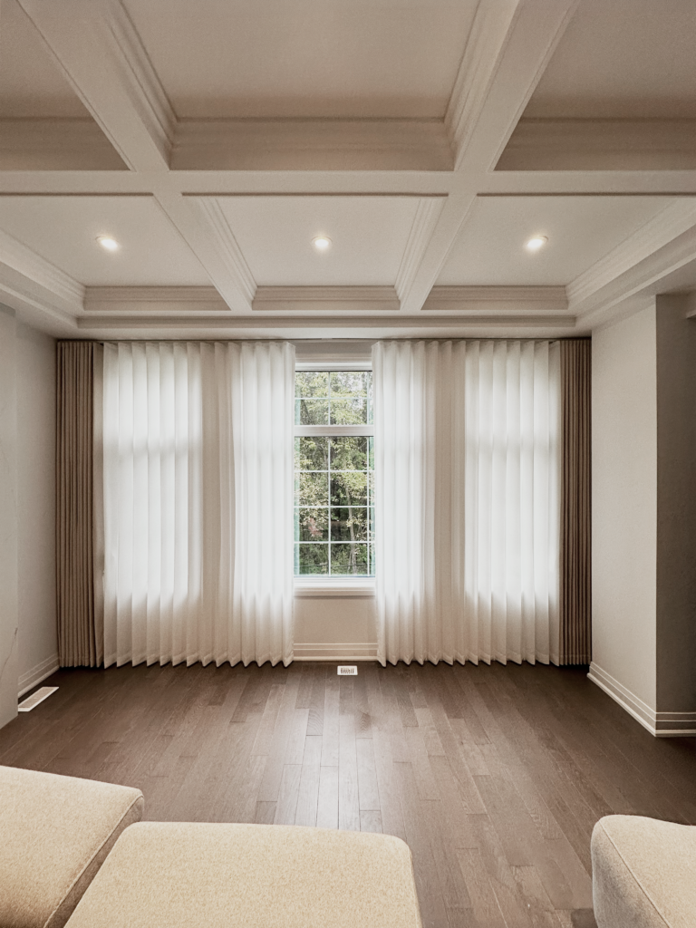 Elegant floor-to-ceiling sheer curtains and pleated drapery panels installed in a luxury Oakville living room with a coffered ceiling.
