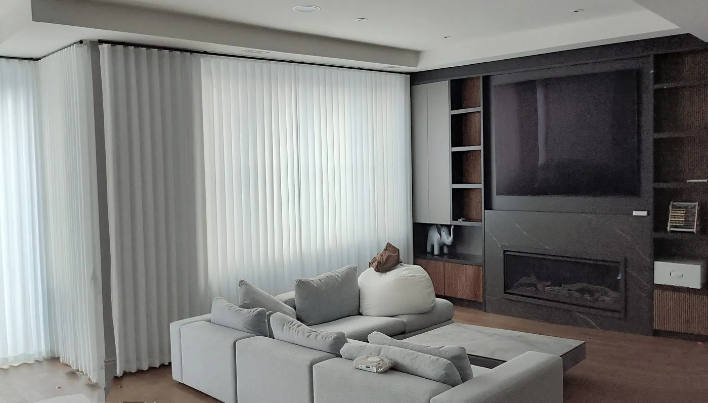 Layered sheer and opaque drapery along a media wall with fireplace in a Toronto home