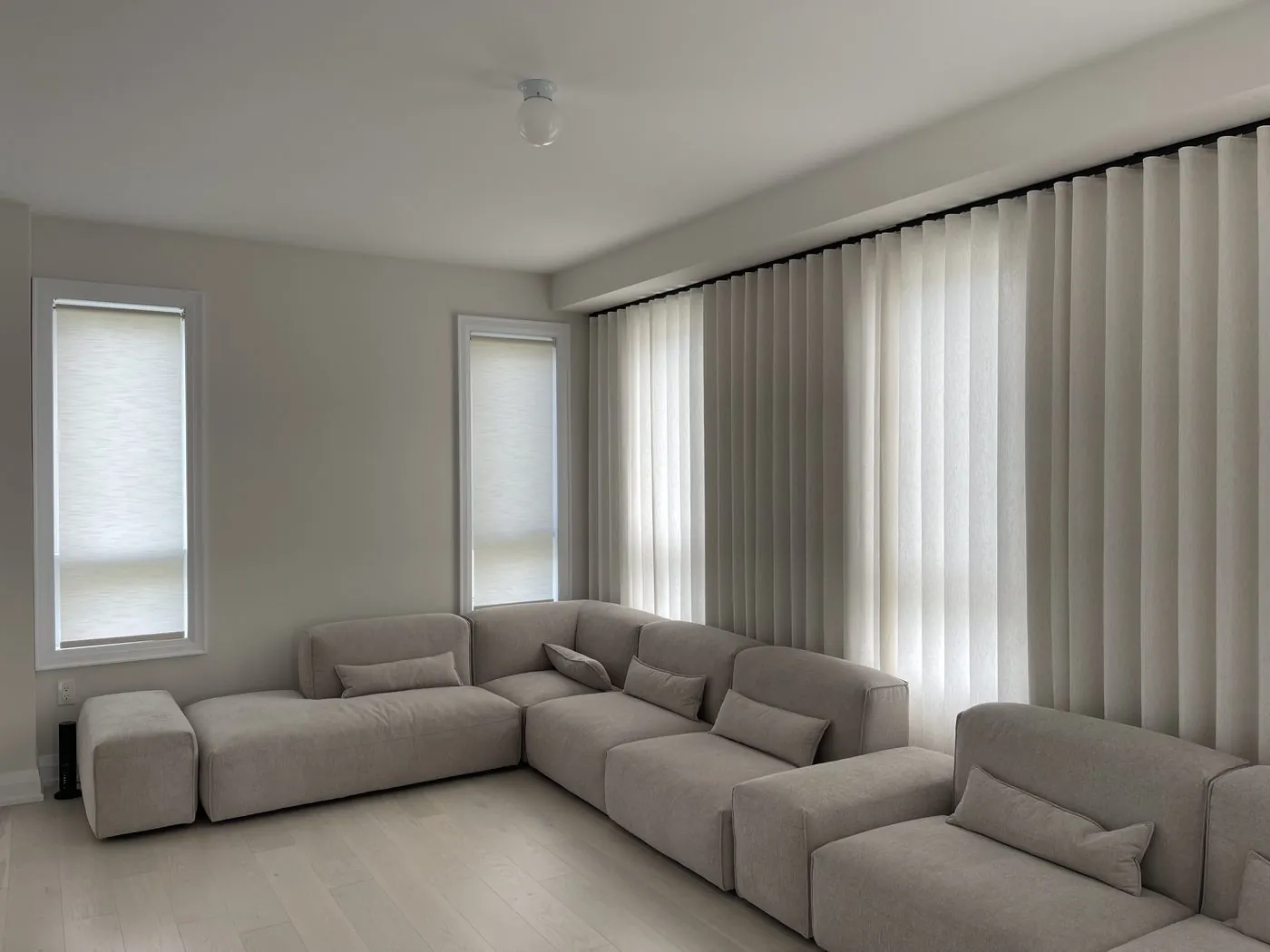 Greige ripplefold sheer curtains wrapping a corner of windows above a low sectional