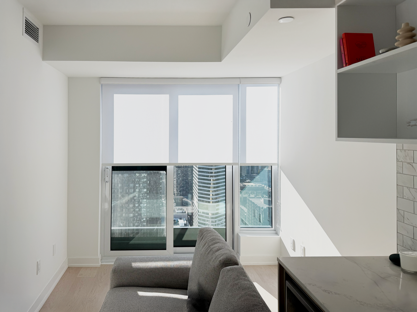 Light-filtering roller shade on floor-to-ceiling glass in a downtown Toronto condo with a city skyline view