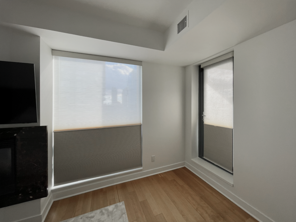 A bright modern room corner with light wood flooring featuring two large windows fitted with top-down bottom-up cellular shades in dual sheer and light-filtering materials.
