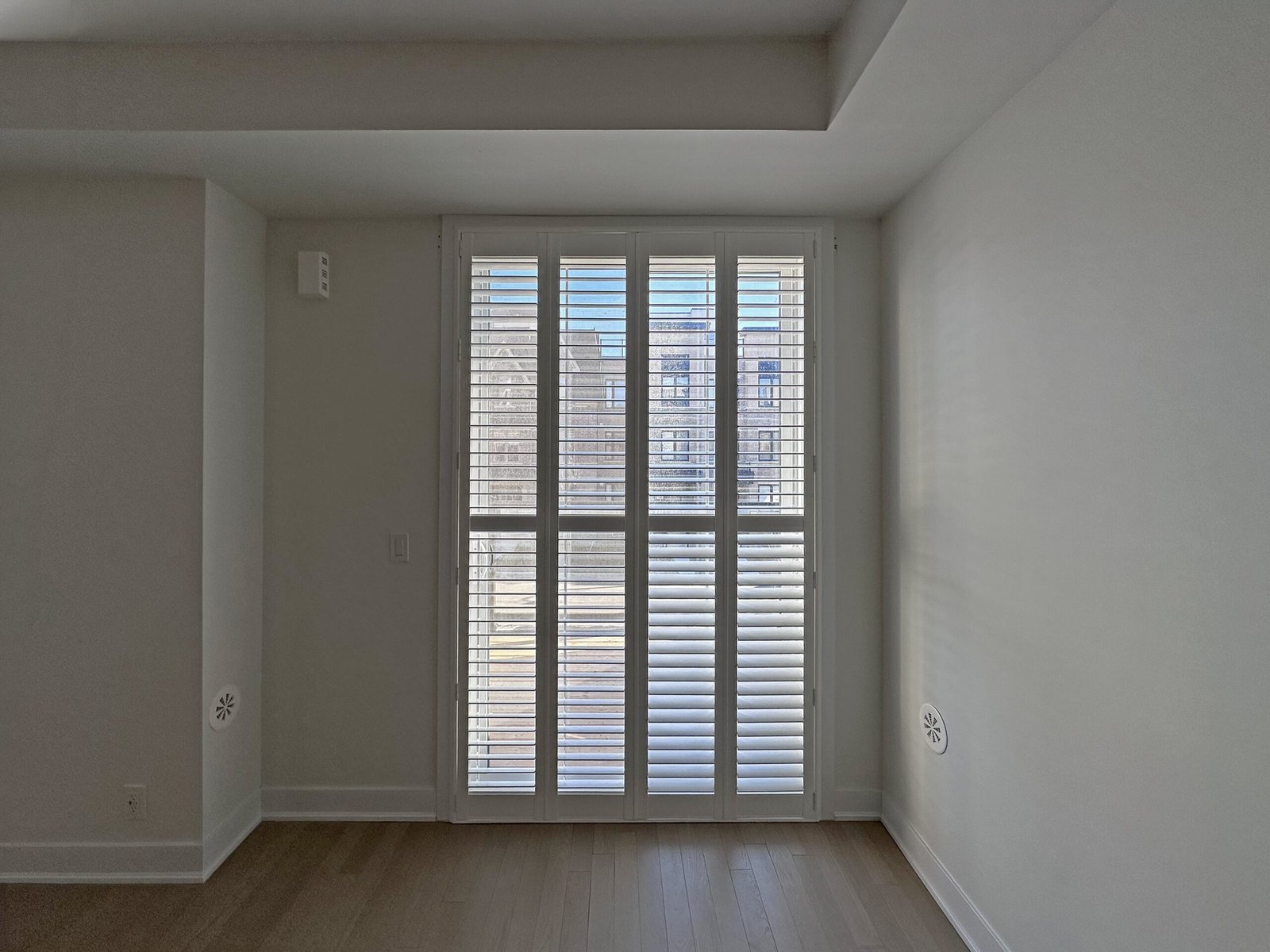 Custom white bi-fold shutters closed across a wide opening in a Toronto home