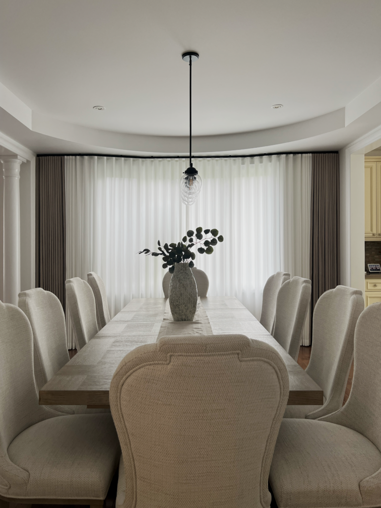 Sheer curtains closed across a dining room bay window, diffusing daylight.