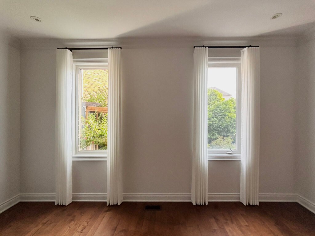 Sheer curtains layered with taupe decorative drapery on a living room bow window.